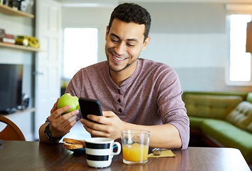 Picture of a man eating an apple looking at his phone.