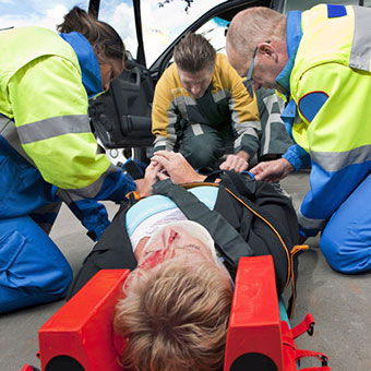 Paramedics and a fireman strapping a wounded woman with a neck brace on a stretcher.