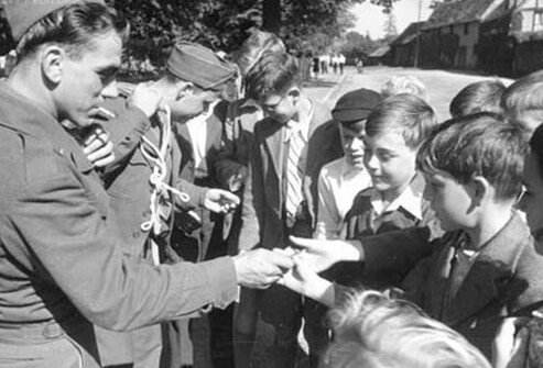 Soldiers hand out chocolate to French children during WWII.