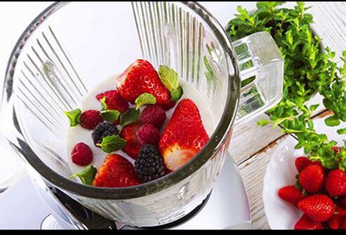 A close up of a blender with mixed berries and milk inside.