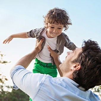 A man spins his son in the air playfully.