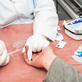 A nurse collects finger blood specimens to test blood glucose levels.