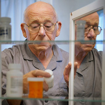 An elderly man taking his kidney medication from the medicine cabinet.