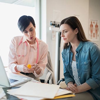 A health-care professional consults with a patient while holding a prescription bottle.