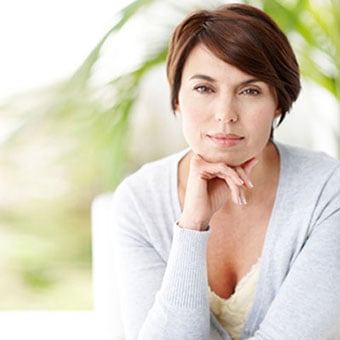A middle-aged woman sits with her chin on her hand.
