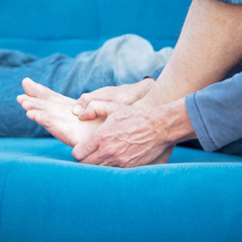 A person sits up in bed with a foot cramp.