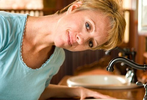 A woman tilting her head over the sink.