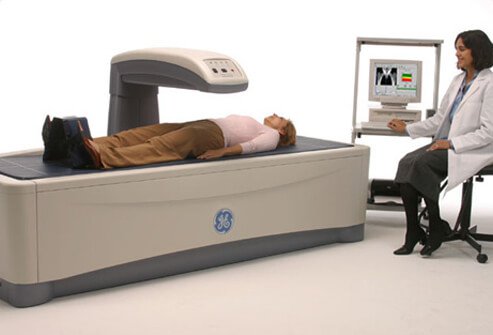 A technician performs a DXA bone density scan on a female patient.