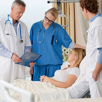 A group of doctors and nurses consulting with patients in a hospital room.