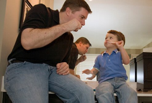 A father shows his son how to brush his teeth.