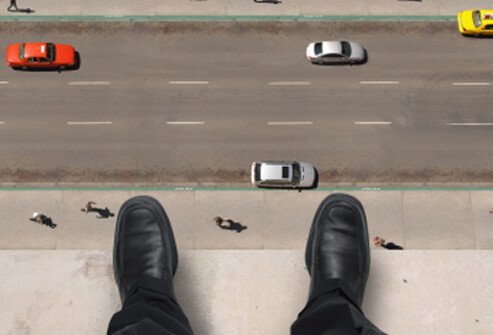 A man on the ledge of a high-rise building looks down to the street below.