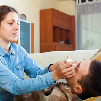 A woman puts eye drops in a man's eye to treat his pinkeye.