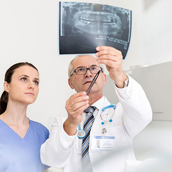 A dentist and his dental assistant review teeth in an X-ray to determine the need for root canal treatment.