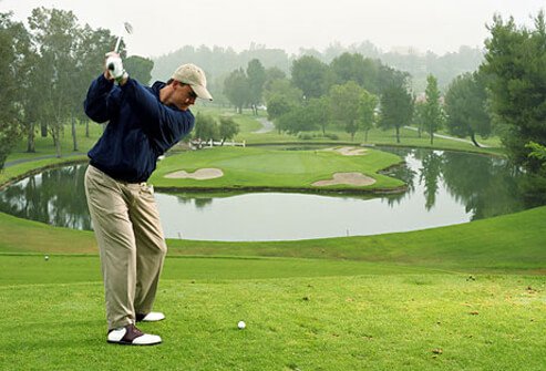 Golfer about to tee off on cool morning, protected from the sun.