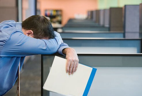 A man with shift work sleep disorder resting his head on an office cubicle.