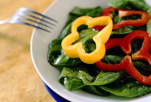 Bowl of spinach topped with bell peppers.