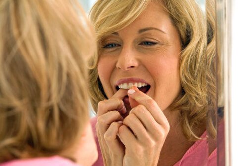 A woman flossing her teeth in the mirror.