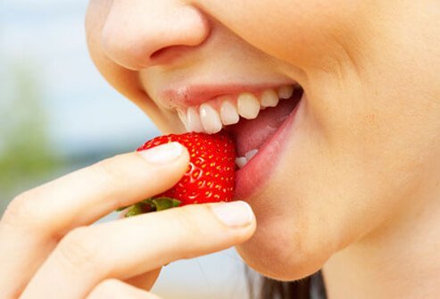 A woman biting into a strawberry.